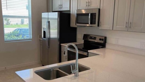 A modern kitchen with stainless steel appliances, a large island with a sink, and light-colored cabinetry. - 2-bedroom, 2/5 bath  townhome in westview  Kissimmee with cool AC, (Kissimmee)