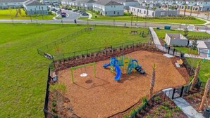 A playground with a slide and swings, surrounded by a fence, in a residential area with houses in the background. - 2-bedroom, 2/5 bath  townhome in westview  Kissimmee with cool AC, (Kissimmee)