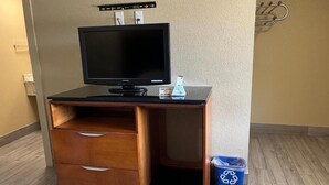 Habitación de hotel con un escritorio de madera, un televisor, un cesto de basura y un gancho en la pared.