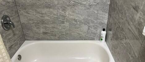 Una bañera con una toalla blanca, una botella de champú y una cortina de ducha.