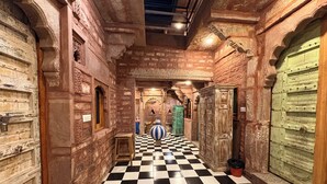 A corridor with checkered flooring, stone walls, and traditional doors.