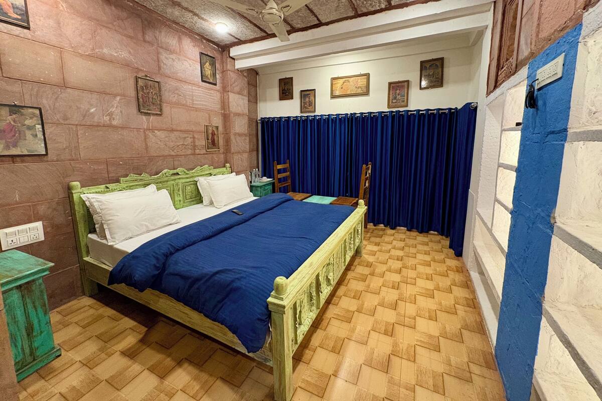 Una habitación con cama, ventilador de techo, piso de madera y una pared con ventana.