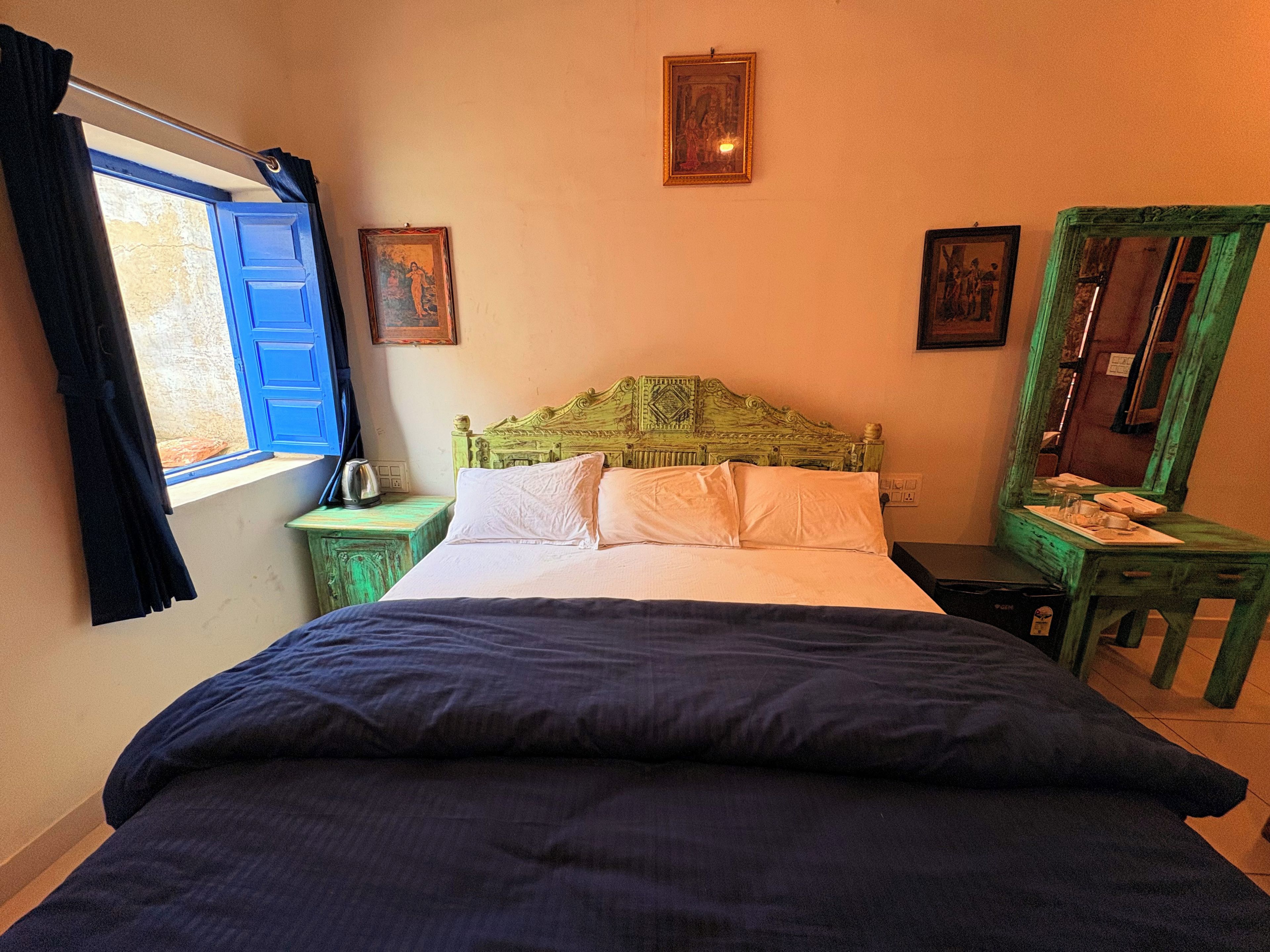 Una habitación con cama, mesita de noche, ventana con cortinas y espejo.