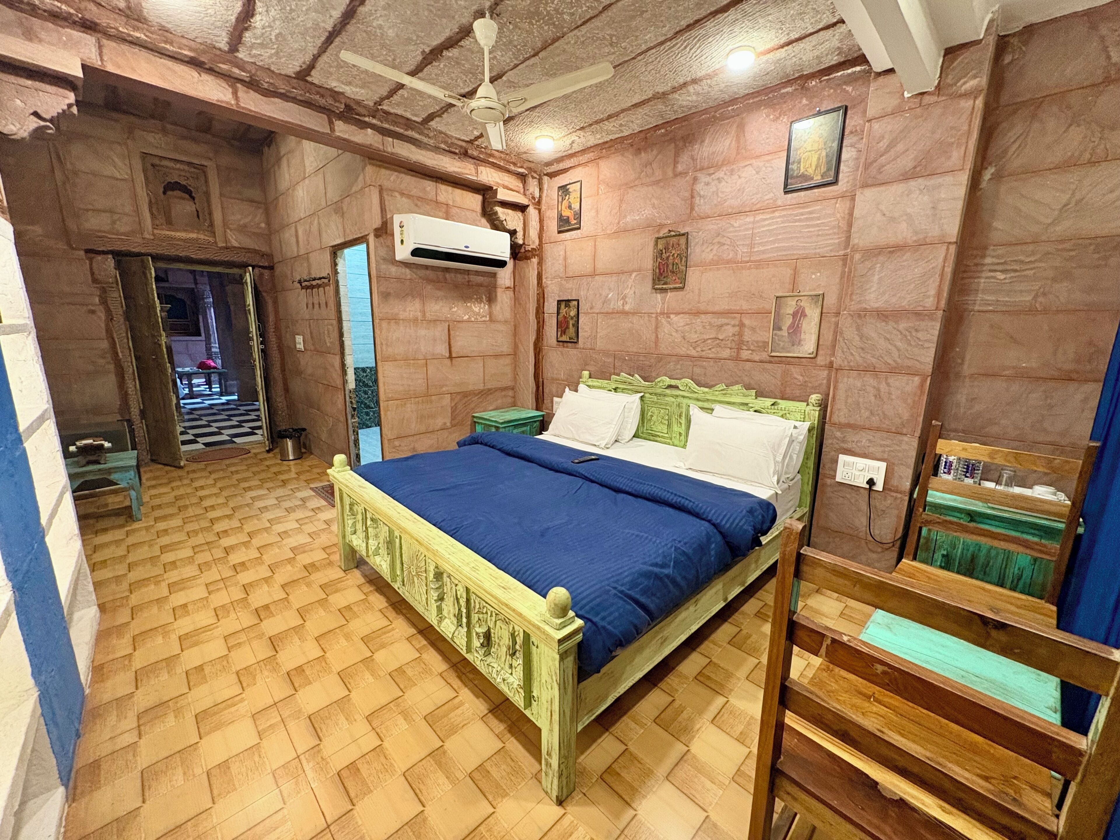 A room with a bed, an air conditioning unit, a ceiling fan, and a small table.