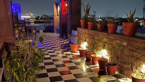 A rooftop terrace with a checkered floor, potted plants, and a view of the cityscape at night.