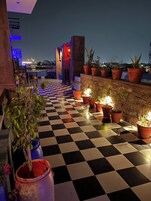 Una terraza en la azotea con suelo a cuadros, plantas en macetas y vista panorámica de la ciudad de noche.