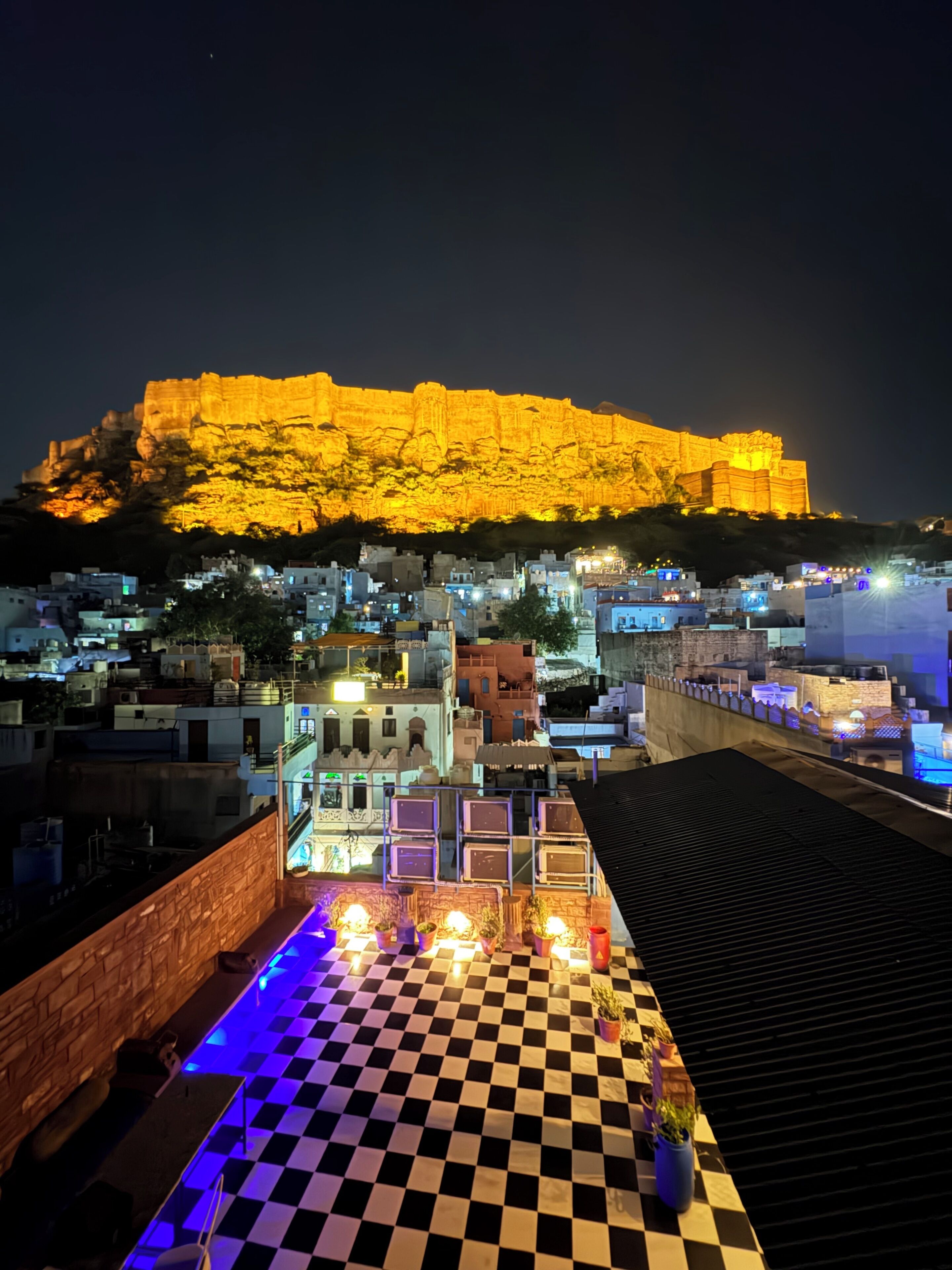 Una terraza en la azotea con piso a cuadros, vista a una fortaleza histórica y edificios circundantes.