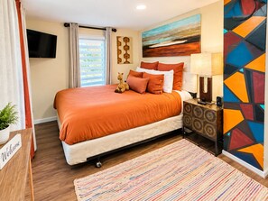 A hotel room with a bed, a TV, a painting, a lamp, and a welcome sign.
