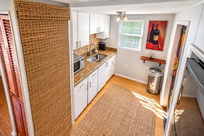 A compact kitchen with white cabinets, a microwave, a sink, and a trash can.