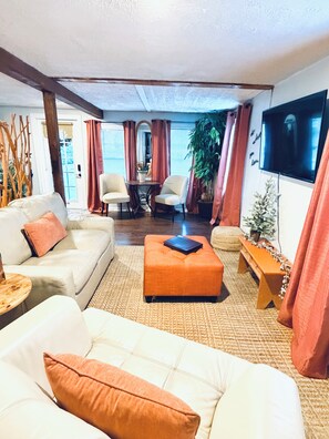 Un salon comprenant un canapé, un pouf, des fauteuils, une table basse, un téléviseur et une plante en pot.