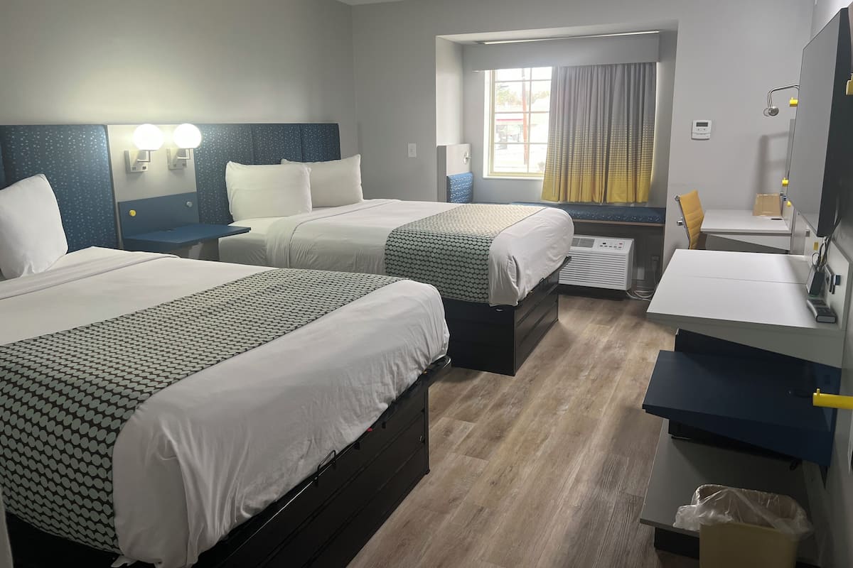 Habitación de hotel con dos camas, un escritorio, una silla, un ventanal con cortinas y un espacio para el baño.