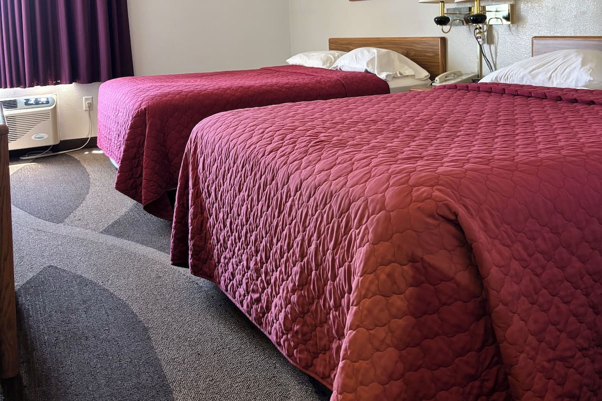 A hotel room with two beds, a desk, a telephone, and a wall-mounted lamp.