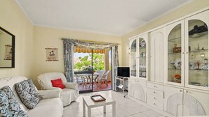A living room with a sofa, a coffee table, a TV, and a cabinet with glass doors. - ‘Férias Vilamoura’ Apartment with Balcony, Wi-Fi and Air Conditioning (Quarteira)
