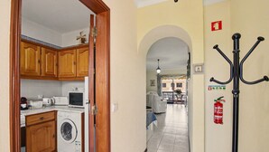 A laundry area with a washing machine, wooden cabinets, and a microwave. - ‘Férias Vilamoura’ Apartment with Balcony, Wi-Fi and Air Conditioning (Quarteira)
