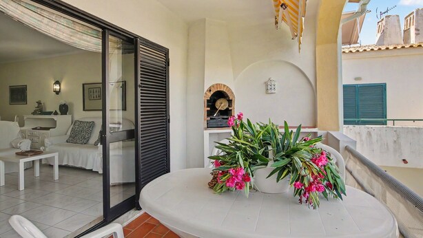 A balcony with a white table, potted plants, and a view of the building's architecture. - ‘Férias Vilamoura’ Apartment with Balcony, Wi-Fi and Air Conditioning (Quarteira)