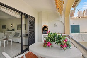 A balcony with a white table, potted plants, and a view of the building's architecture. - Leme Apartment – Balcony, Wi-Fi & Air Conditioning (Quarteira)
