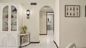 A hallway with a white cabinet, a wall-mounted light, a clock, and a framed picture. - ‘Férias Vilamoura’ Apartment with Balcony, Wi-Fi and Air Conditioning (Quarteira)