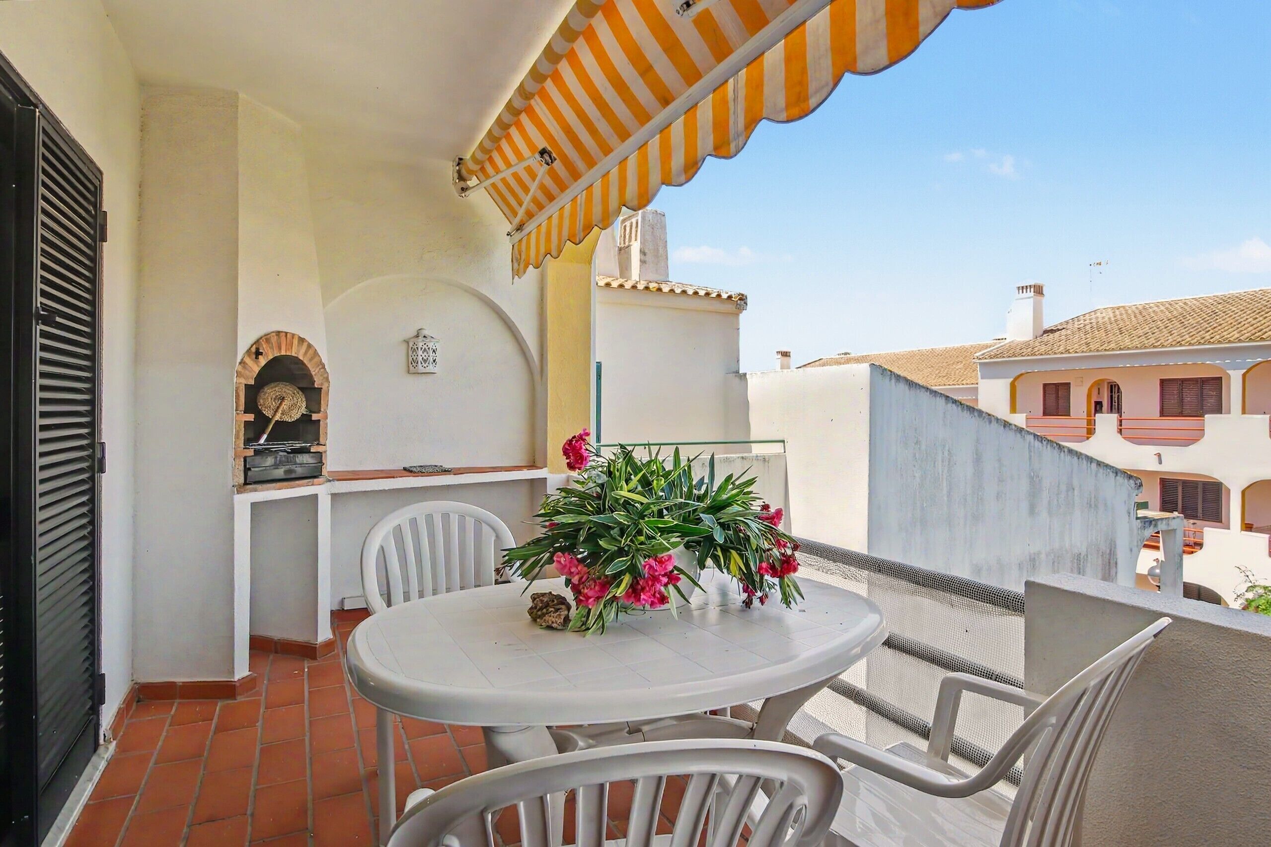 A balcony with a table, chairs, a potted plant, and a striped awning.