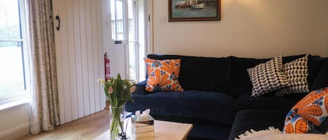 A living room with a dark blue sofa, patterned cushions, a wooden coffee table with a vase and a book, and a painting on the wall.
