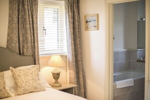 Ein Schlafzimmer mit einem Bett, einem Nachttisch mit Lampe, gemusterten Vorhängen und einem Badezimmer mit Dusche und Handtuchhalter.