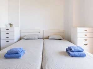 A double bed with striped bedding, two pillows, a small bedside table, and a dresser with drawers. - Tramuntana II by Interhome (Salou)