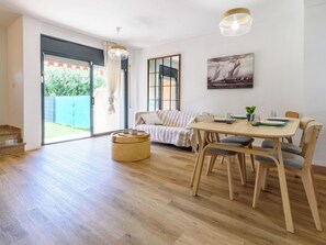A modern living room with a sofa, dining table, and chairs, a large window with curtains, and a painting on the wall. - Tramuntana II by Interhome (Salou)