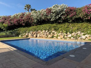 A swimming pool with clear blue water, surrounded by a stone wall and a variety of flowering plants. - Tramuntana II by Interhome (Salou)