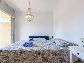 A bedroom with a bed, a bedside table, a hanging light fixture, and a window. - Tramuntana II by Interhome (Salou)