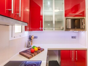 A kitchen with red cabinets, a microwave, and a wooden cutting board with vegetables. - Sant Eloi by Interhome (Tossa de Mar)