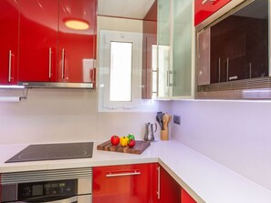 A modern kitchen with red cabinets, a built-in oven, and a window above the sink. - Sant Eloi by Interhome (Tossa de Mar)