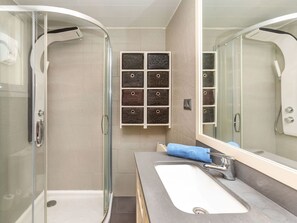Ein Badezimmer mit Duschkabine aus Glas, einem Waschbecken mit Spiegel und Ablagekörben an der Wand.