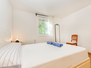 Ein Schlafzimmer mit einem Bett, einem Nachttisch, einem Sessel, einem Heizkörper und einem Fenster mit Vorhängen.