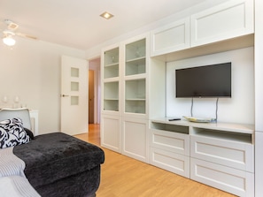 A modern room with a TV, built-in shelving, a seating area, and a door leading to another room. - Sant Eloi by Interhome (Tossa de Mar)