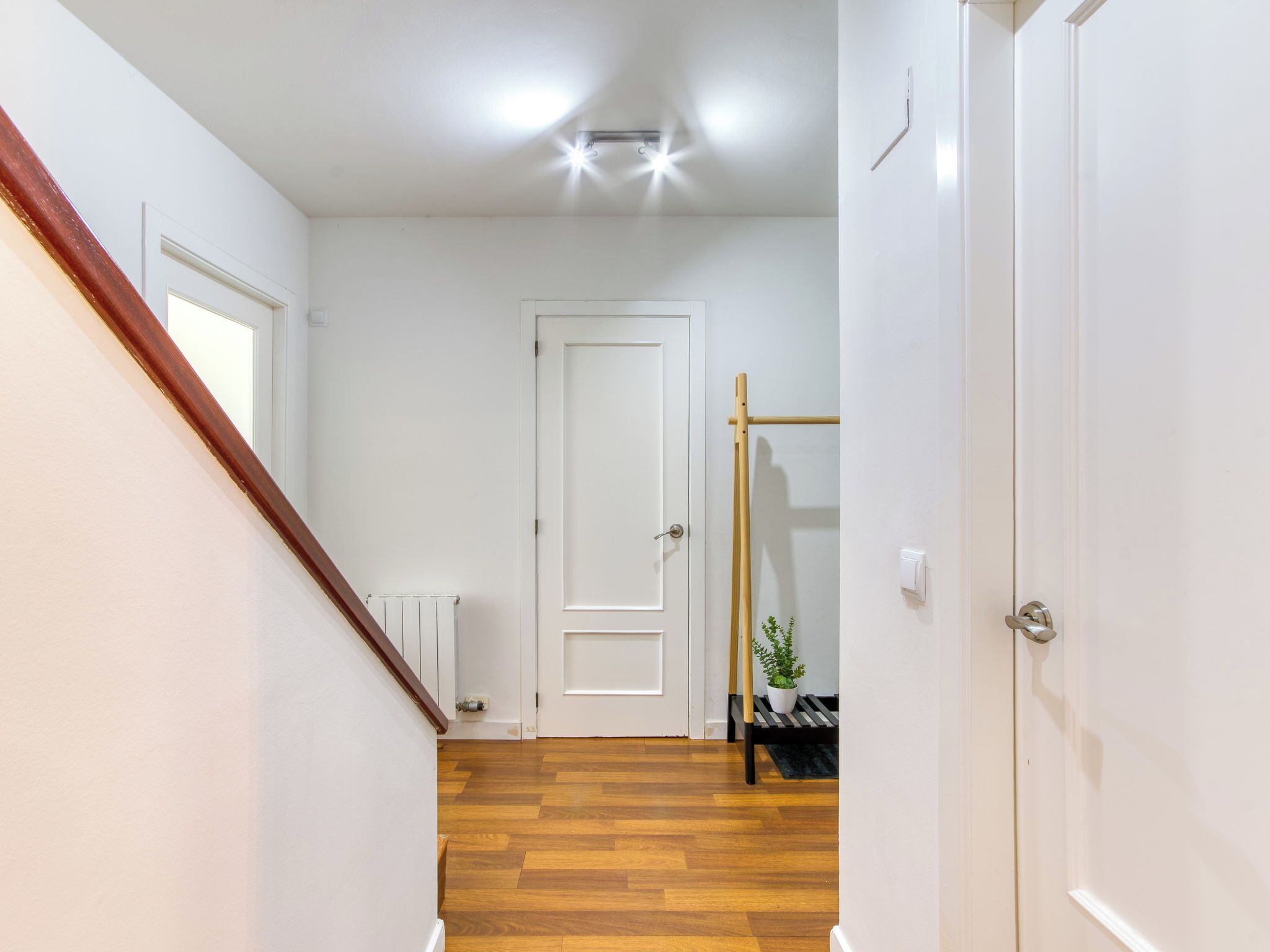 A hallway with a wooden floor, white walls, a white door, and a radiator.