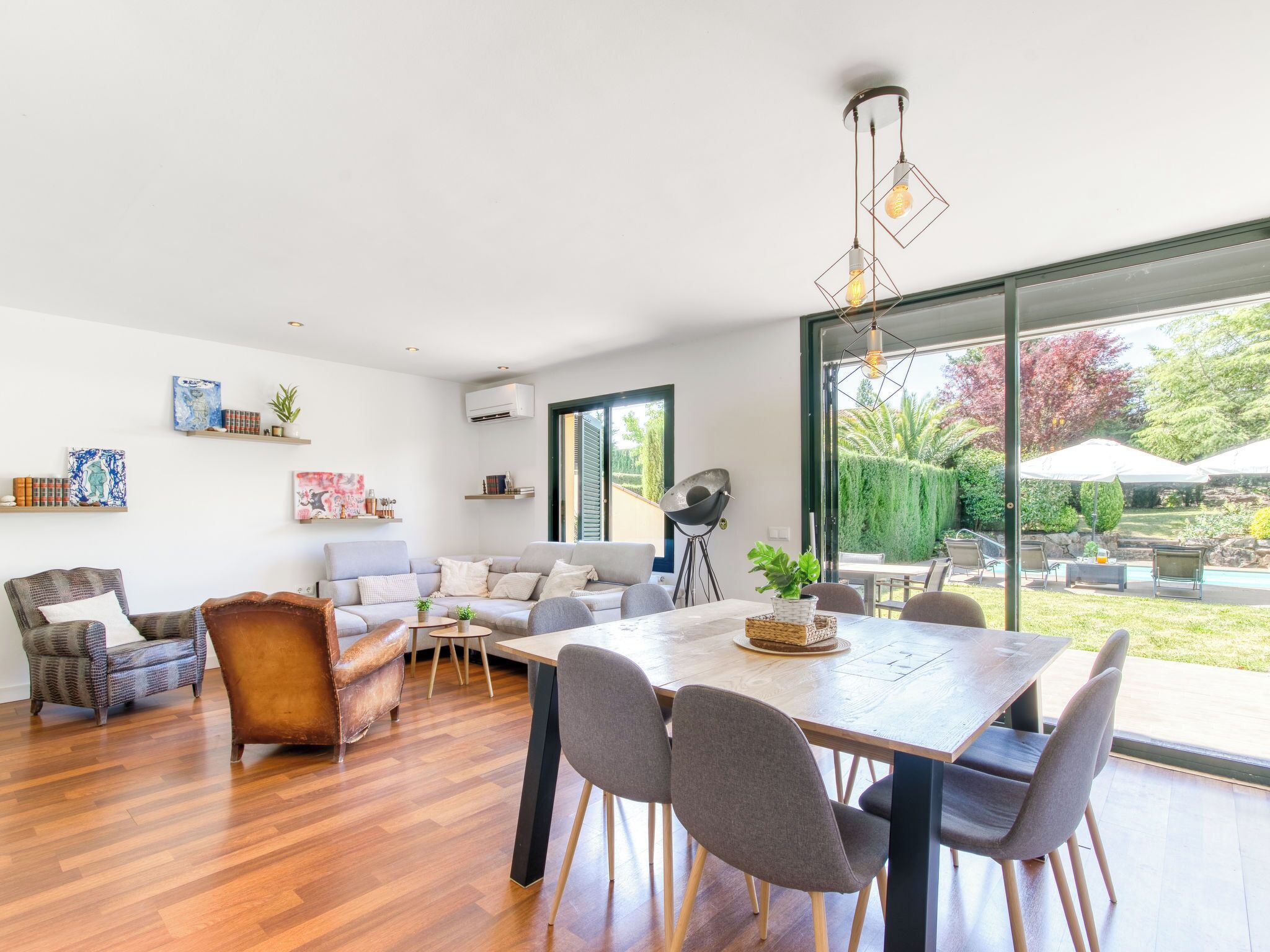 Un salon moderne avec un plancher en bois, un canapé, une table à manger avec des chaises et une grande fenêtre donnant sur l’extérieur.