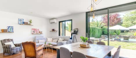 Una sala de estar moderna con piso de madera, un sofá, una mesa de comedor con sillas y un amplio ventanal con vistas al exterior.