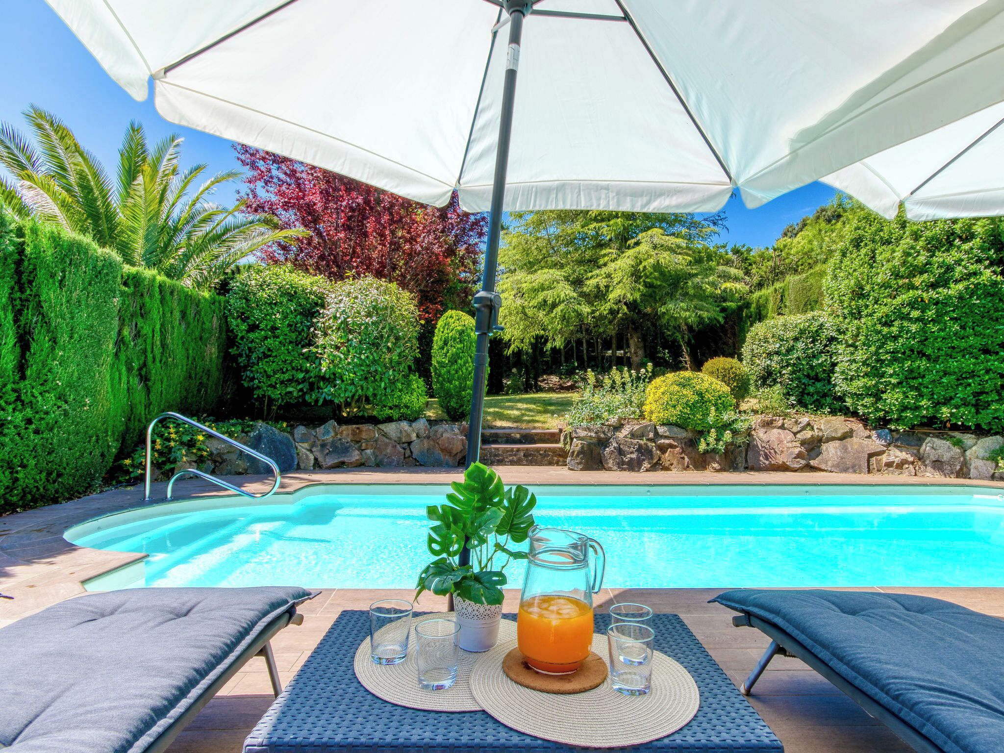 A poolside area with lounge chairs, a table with drinks, and a large umbrella.
