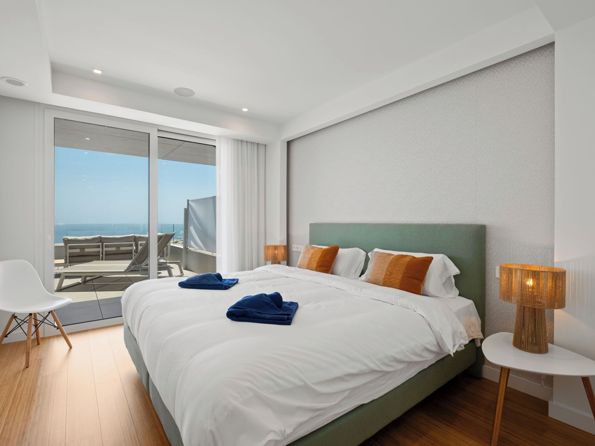 Une chambre d’hôtel moderne avec un grand lit, un balcon offrant une belle vue et une petite table avec une lampe.