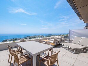 Eine Terrasse mit Tisch, Stühlen und einer Sitzecke, mit Blick auf das Meer und die Stadt.