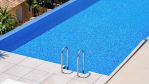 A swimming pool with clear blue water, two metal ladders, and a tiled deck. - Blue Infinity I by Interhome (Moraira)
