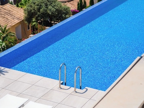 Ein Schwimmbecken mit klarem, blauem Wasser, zwei Metallleitern und einer gefliesten Poolterrasse.
