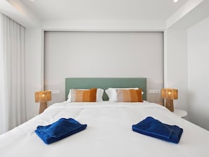 Ein Hotelzimmer mit einem großen Bett, zwei Nachttischlampen, einem grünen Kopfteil und zwei blauen Handtüchern.