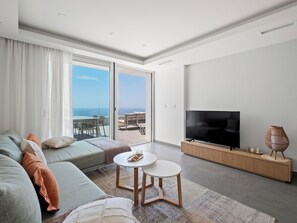 A modern living room with a sofa, a TV, and a balcony with a view. - Blue Infinity I by Interhome (Moraira)