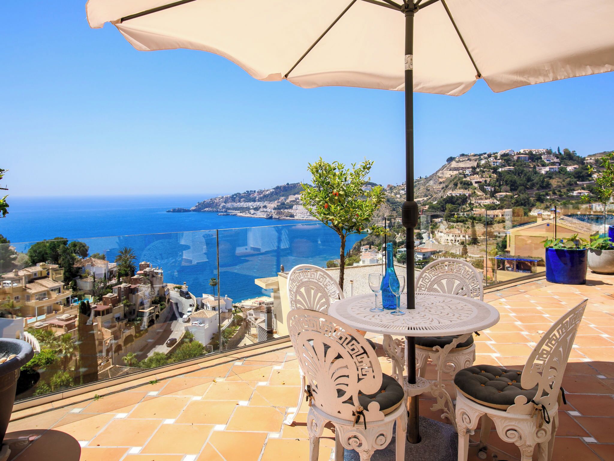 Une terrasse avec une table et des chaises, offrant une vue sur une ville côtière et la mer.