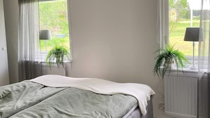 Een slaapkamer met een bed, twee ramen met gordijnen en twee potplanten.