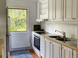 A compact kitchen with white cabinets, a built-in oven, a sink, and a window with a view of greenery. - 4 Person Holiday Home in Hacksvik (Håcksvik)