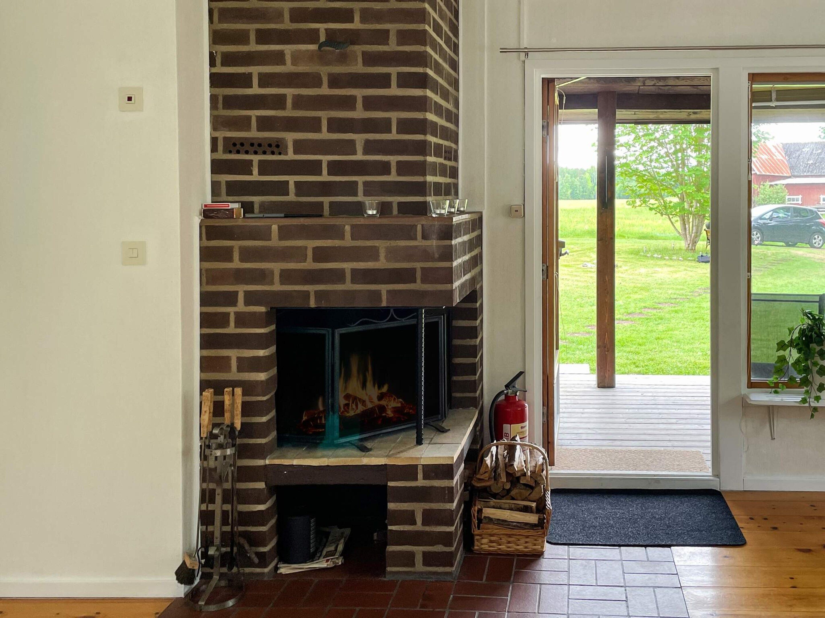 A fireplace with a brick exterior, a fire burning inside, and a door leading to a covered outdoor area.