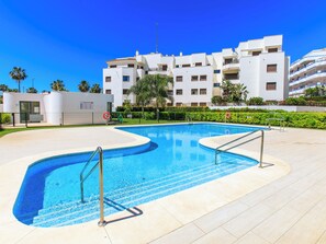 A swimming pool with a curved design, surrounded by a tiled deck. In the background, there are multi-story buildings with balconies. - Sea Garden by Interhome (Torrox Costa)