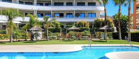 A hotel with a swimming pool, palm trees, and a multi-story building.