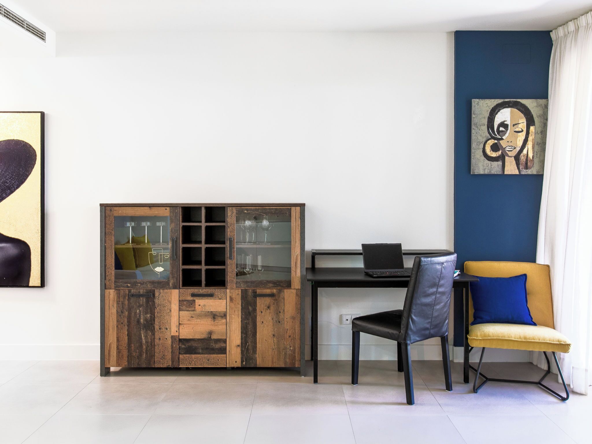 Habitació moderna amb un armari de fusta, un escriptori amb un ordinador portàtil, una cadira i una paret decorativa blava.